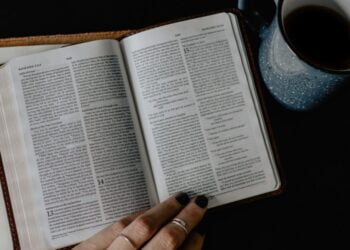 person reading book beside white ceramic mug with coffee