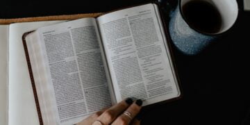 person reading book beside white ceramic mug with coffee