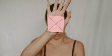 Unrecognizable young woman demonstrating prohibition sign showing gesture of refuse using hand and note with sign stop